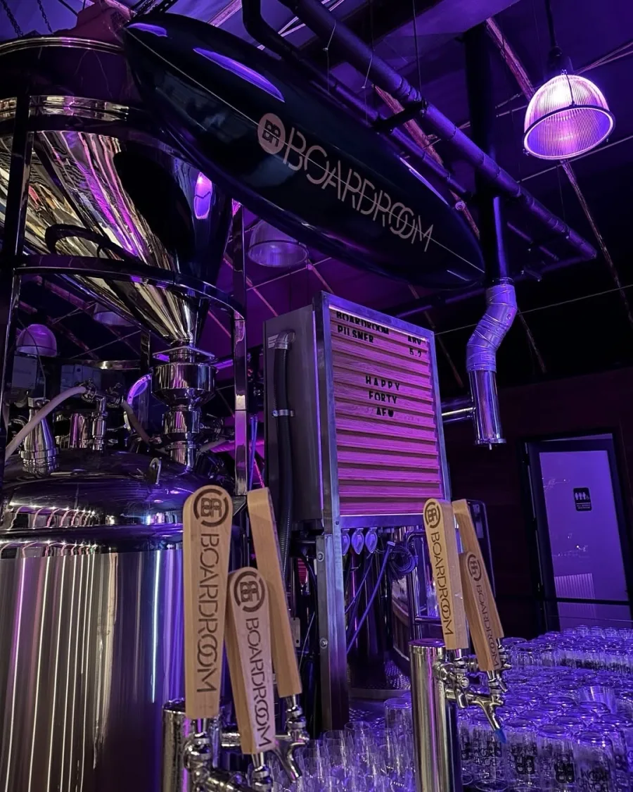 The Boardroom brewhouse: tanks, tap handles, and the surfboard over the bar